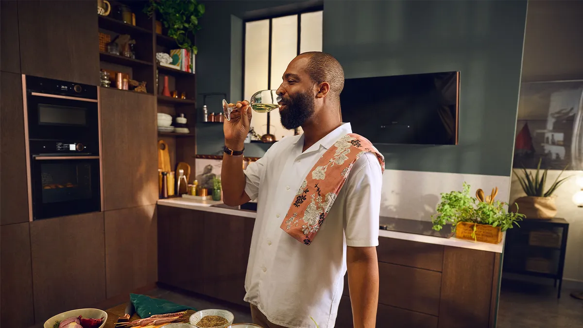 A man enjoying a glass of wine while standing in a modern kitchen. 