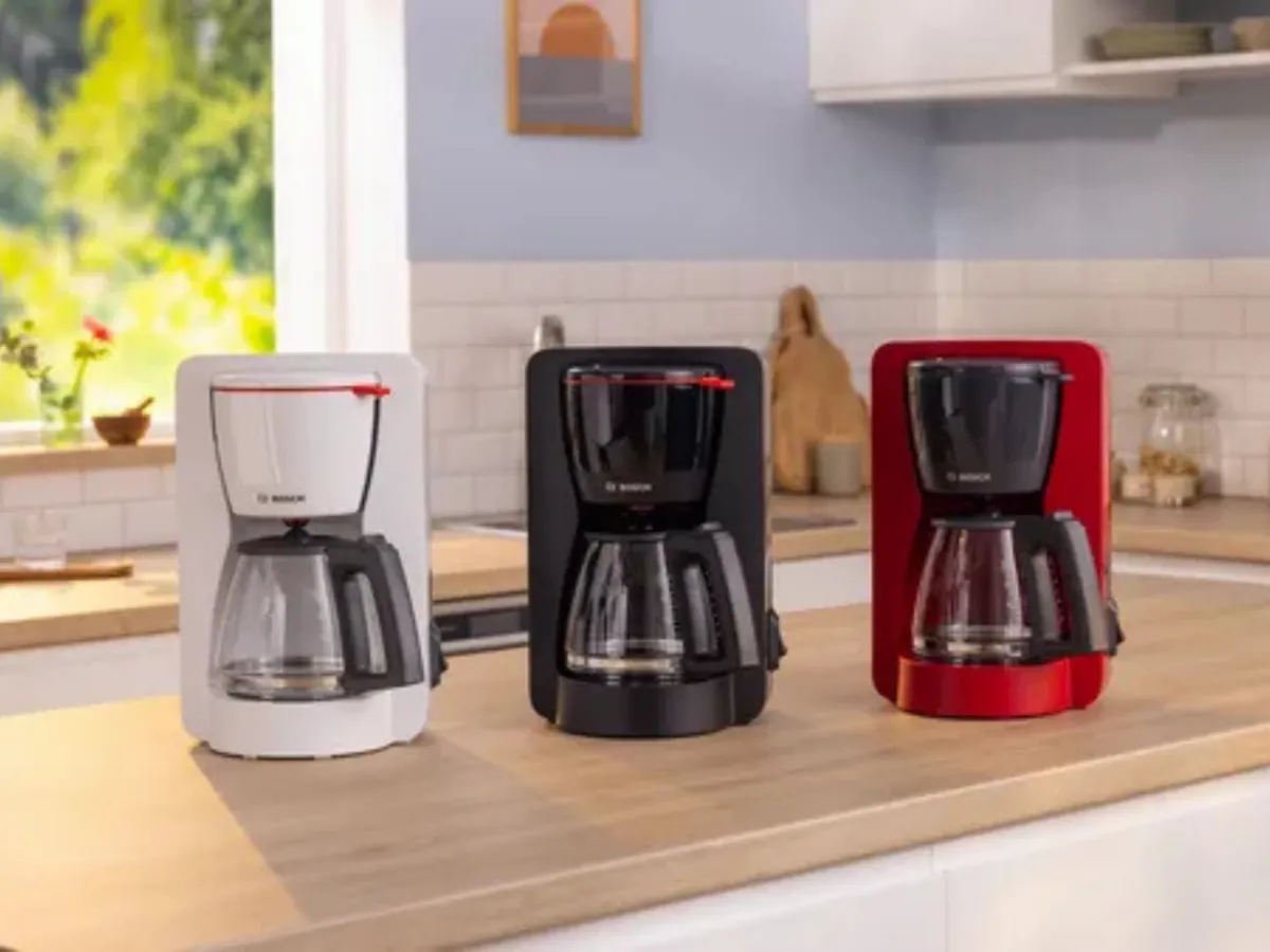 Cafetera de filtro con jarra de café junto a tazas en la encimera de la cocina.