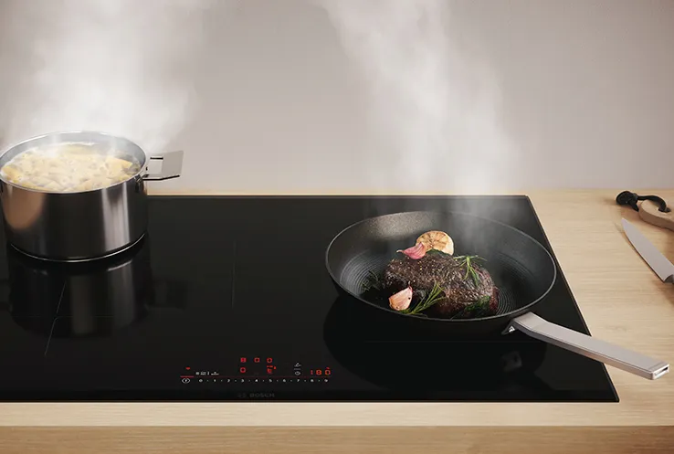 Kitchen with an induction hob cooking a steak with steam rising and vegetables nearby with a signpost icon. 