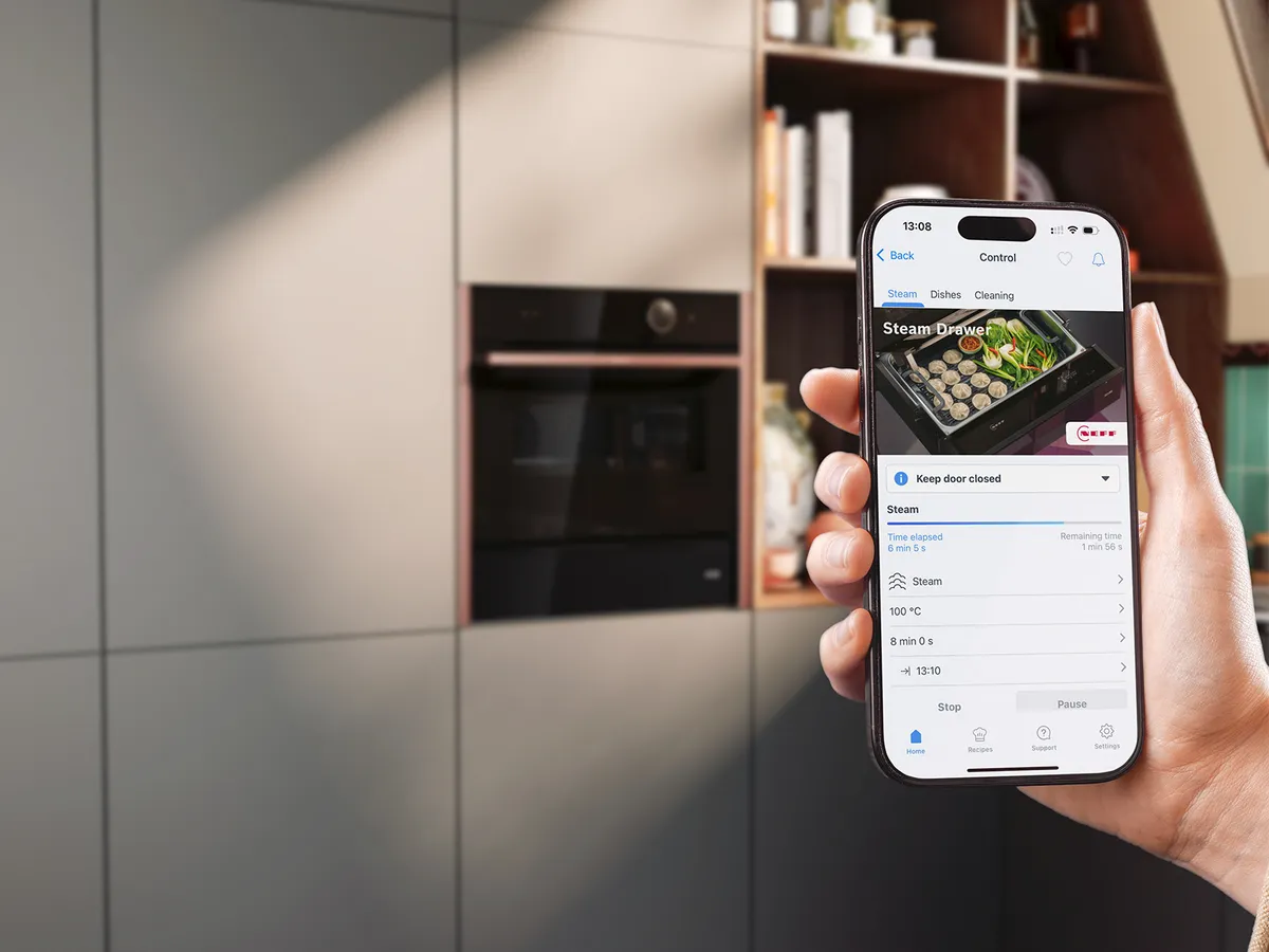 Eine Person hält ein Smartphone, das den Dämpfekomfort eines verbundenen Küchengeräts anzeigt.