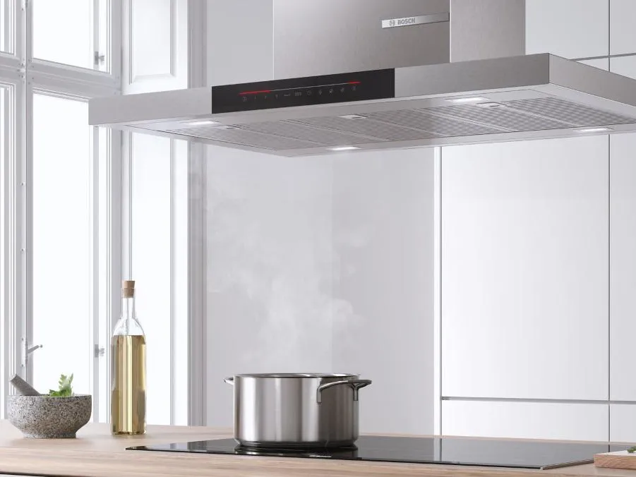 Une scène de cuisine moderne mettant en vedette une élégante hotte de cuisinière en acier inoxydable au-dessus d'une casserole émettant de la vapeur sur un comptoir en bois.