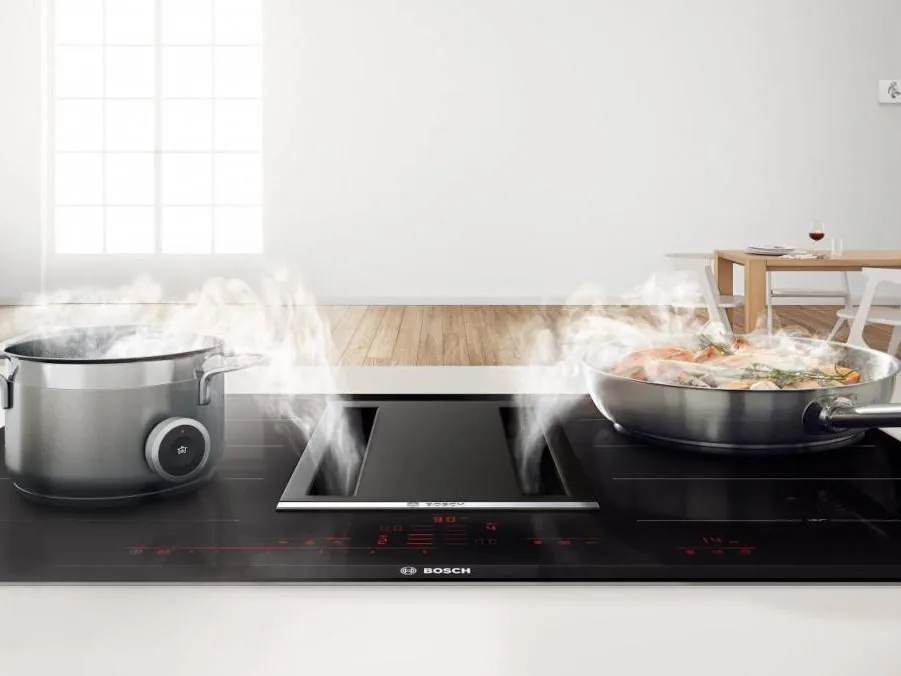 Une table de cuisson à induction moderne avec une casserole d'eau bouillante et une poêle à frire, toutes deux émettant de la vapeur, installées dans une cuisine lumineuse.