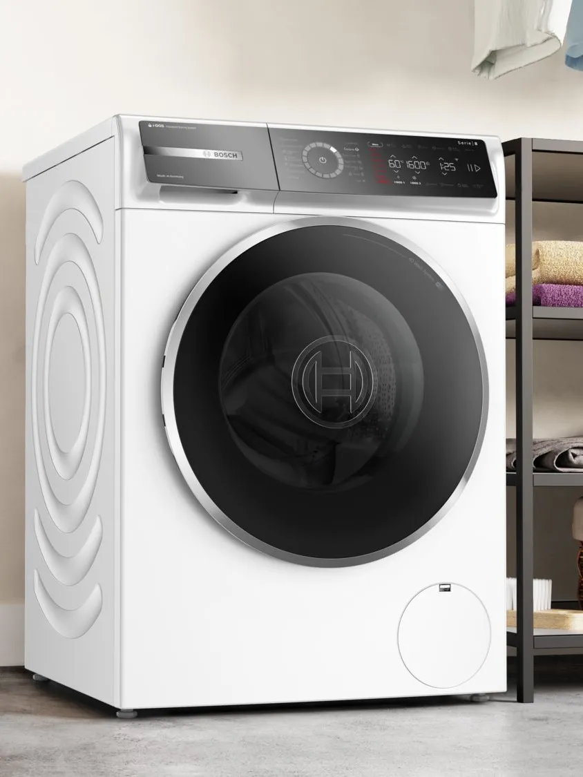 O mașină de spălat Bosch modernă, albă, cu un design elegant cu încărcare frontală, comenzi digitale și o ușă mare din sticlă, expusă într-o cameră de rufe stilată.