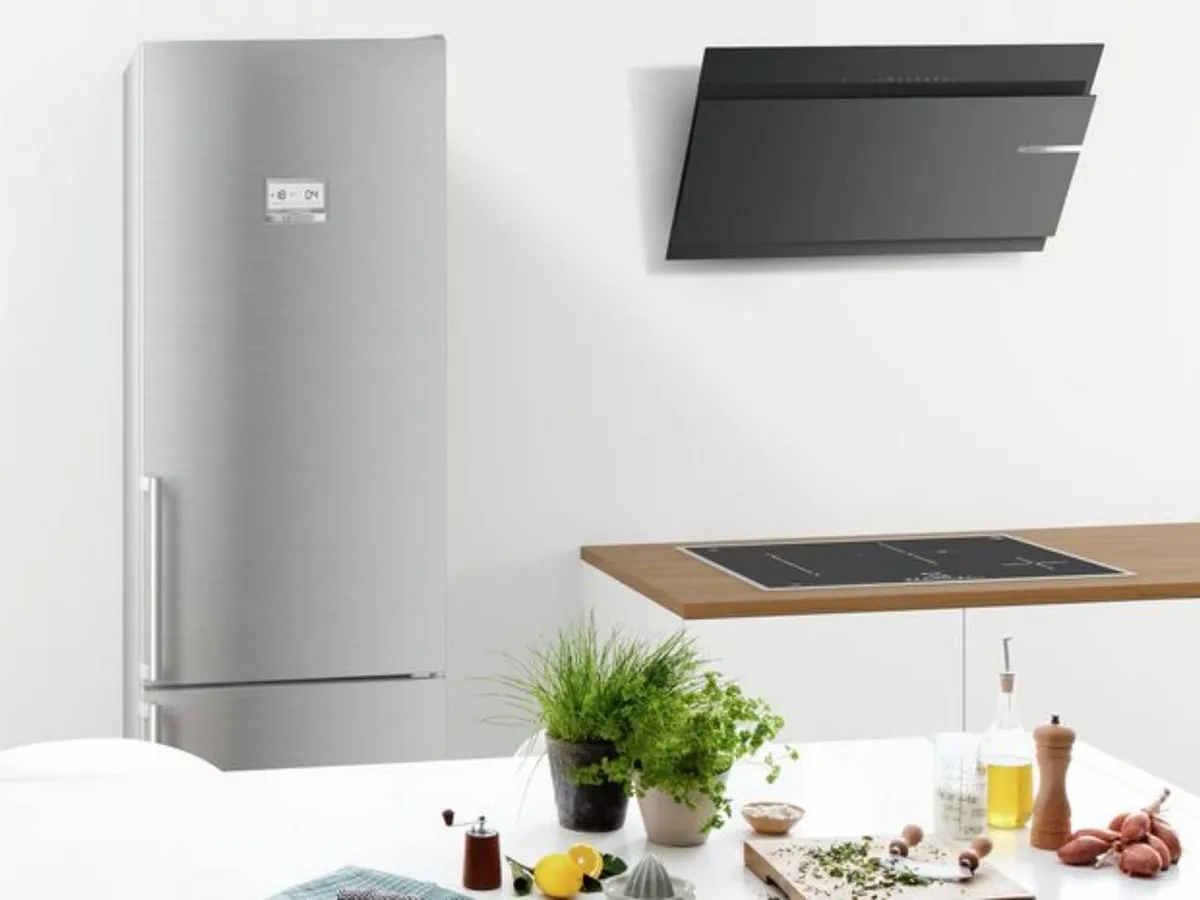 Une cuisine moderne avec un réfrigérateur en inox, une hotte murale noire et une plaque de cuisson.
