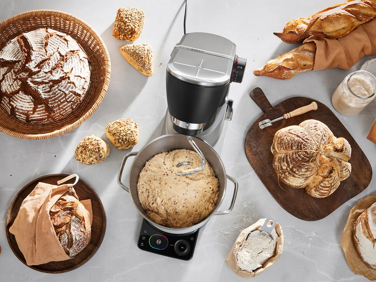 Top-Ansicht der Serie 8 Küchenmaschine auf der Arbeitsplatte, während sie mit dem Knethaken in Gebrauch ist. Verschiedene Backwaren befinden sich auf Tabletts rundherum.