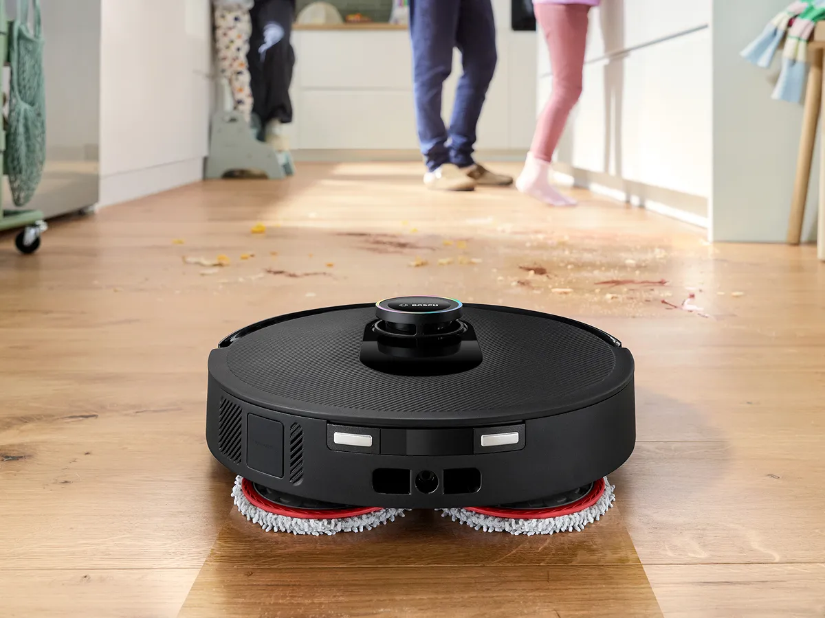 Spotless cleaning robot mopping on hardwood floor in a bright room with family in background.