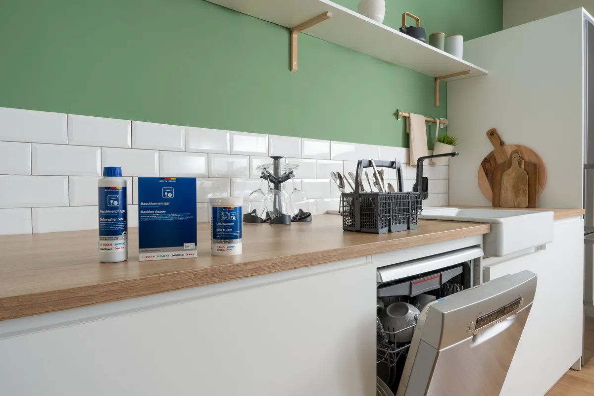 Cleaning and descaling products on a kitchen counter with a dishwasher door open in the background