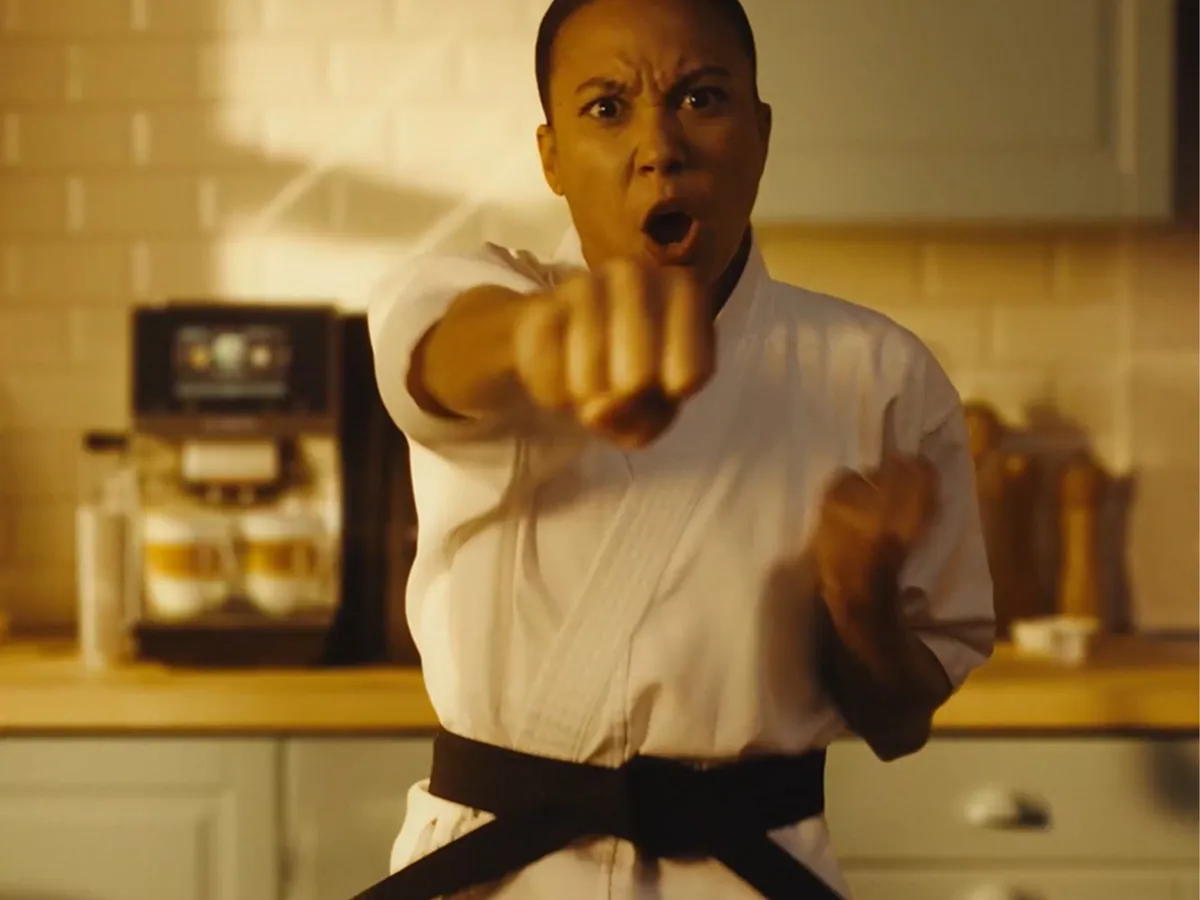 A sleek coffee machine serves a latte in a glass cup, beside a wooden stand with cookies and a mug, in a bright kitchen setting.