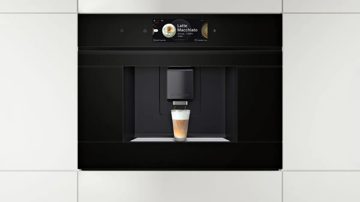 Built-in coffee machine next to built-in oven in a white interior kitchen.