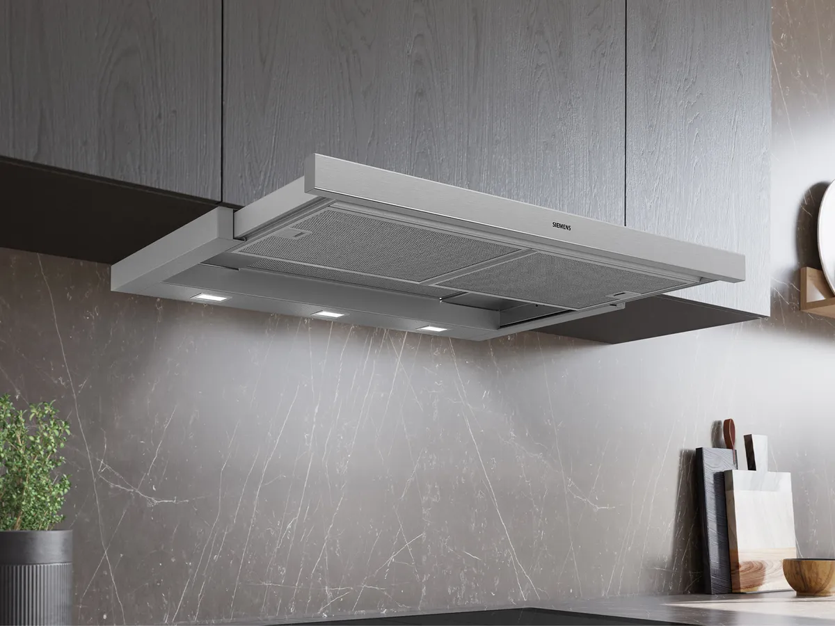 A sleek, modern Siemens kitchen hood installed beneath wooden cabinets, with smoke rising and LED lights illuminating the area below.