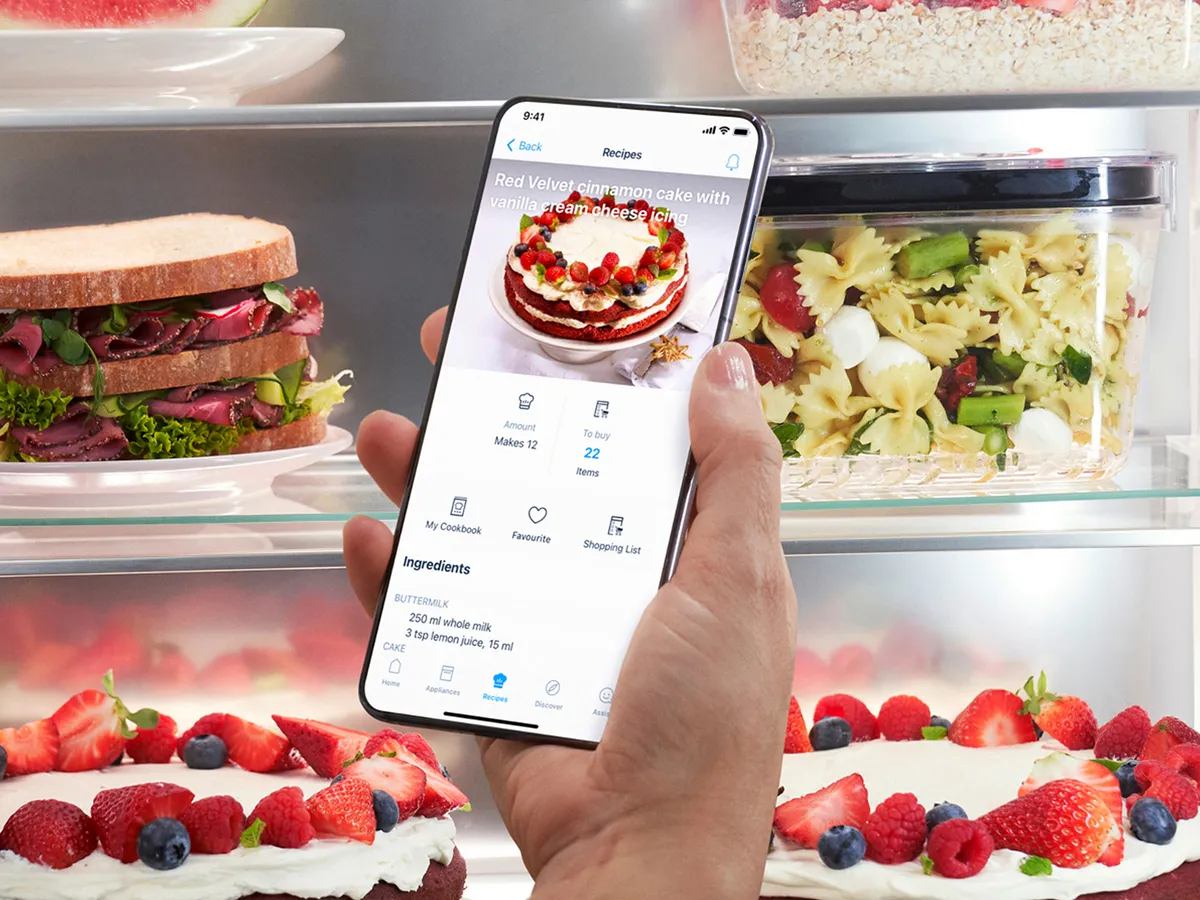 A person holding a smartphone in front of a Bosch French door fridge freezer, showcasing its features and design.