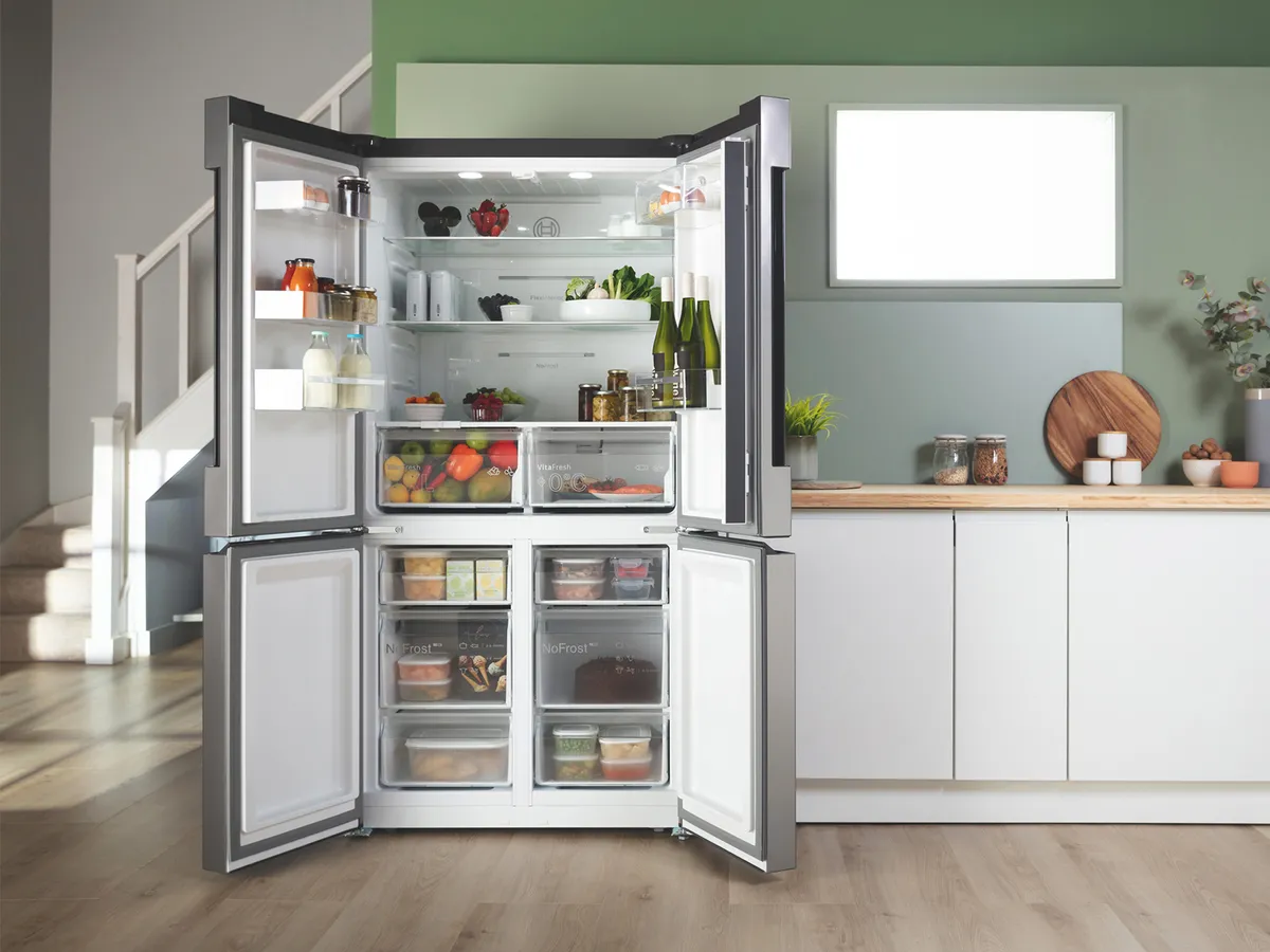 Open refrigerator filled with various food items, including fruits, vegetables, and condiments, in a modern kitchen setting.