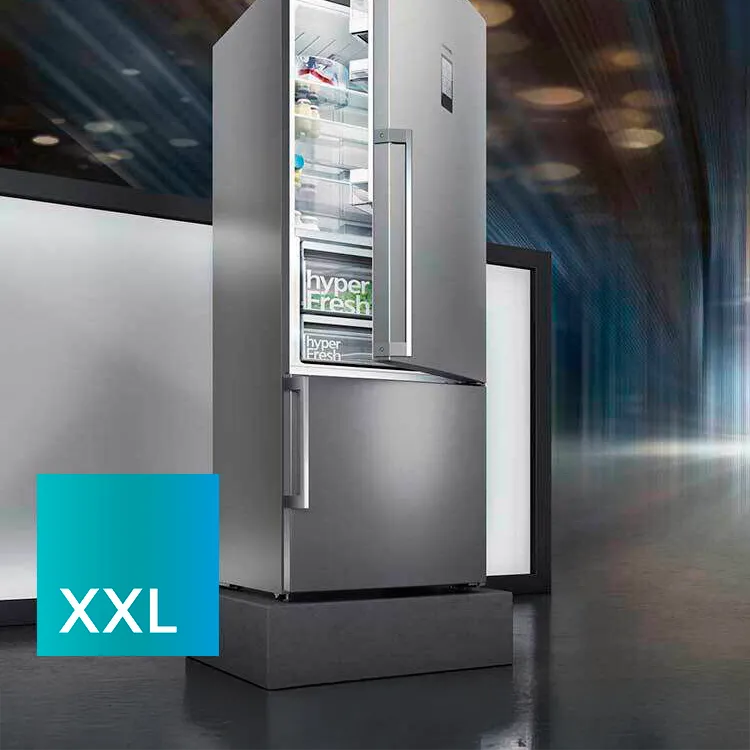 Moderni hopeanvärinen jääkaappi avattuna, jossa näkyy elintarvikkeita. Taustalla on blurred valomerkkejä ja kaksi näyttöä, joista toinen on merkitty "XXL