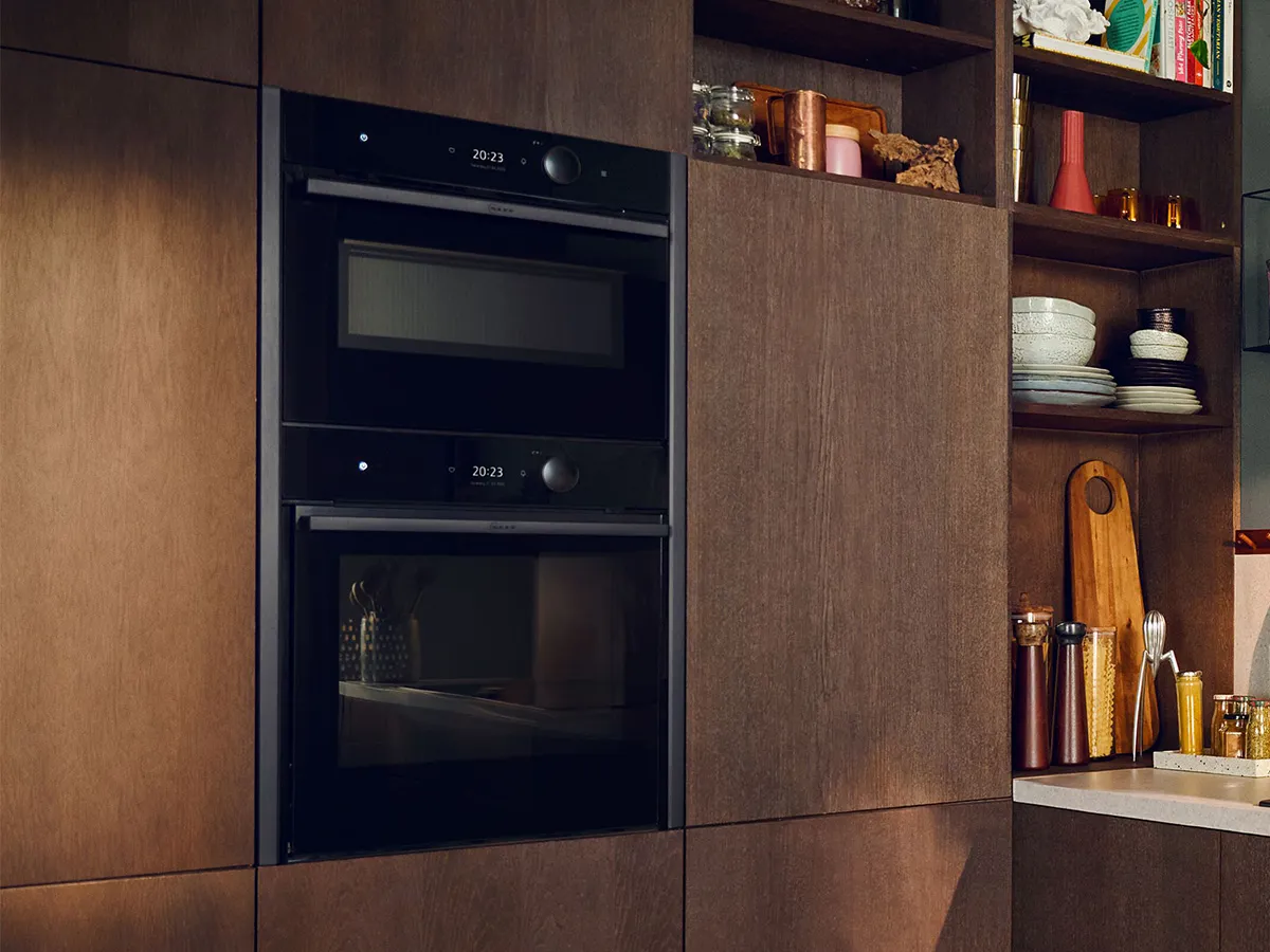 Two ovens in Brushed Bronze stacked on top of each other in dark brown wood kitchen 