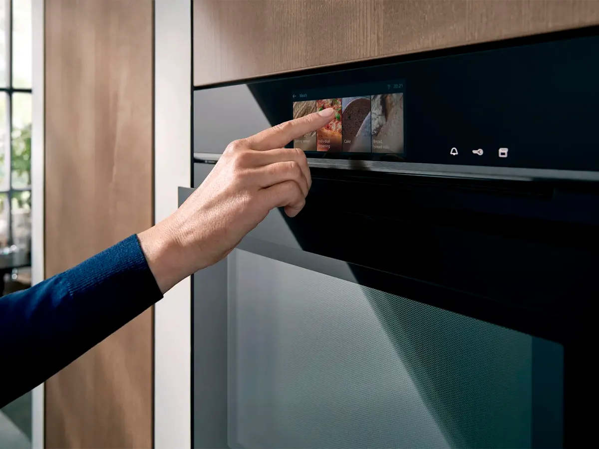 Person interacting with a touchscreen on a modern built-in oven in a kitchen setting.