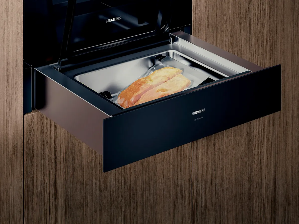 Tiroir chauffant Siemens contenant des aliments dans un sachet sous vide, devant un panneau de bois en arrière-plan.