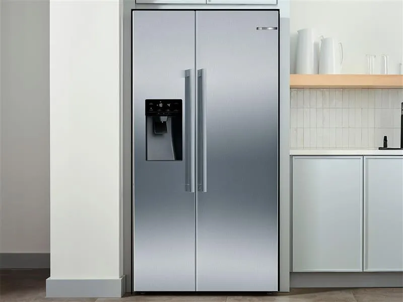 Modern Silver Bosch refrigerator with double doors, next to a light wood kitchen cabinet.