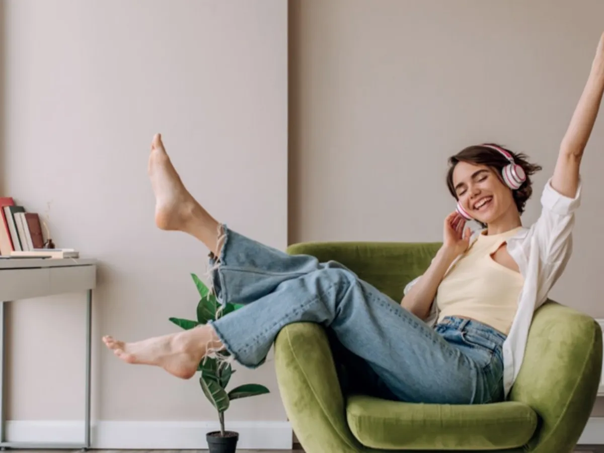 Μια χαρούμενη κοπέλα που κάθεται σε μια χακί πολυθρόνα ακούγοντας μουσική στα ακουστικά της.