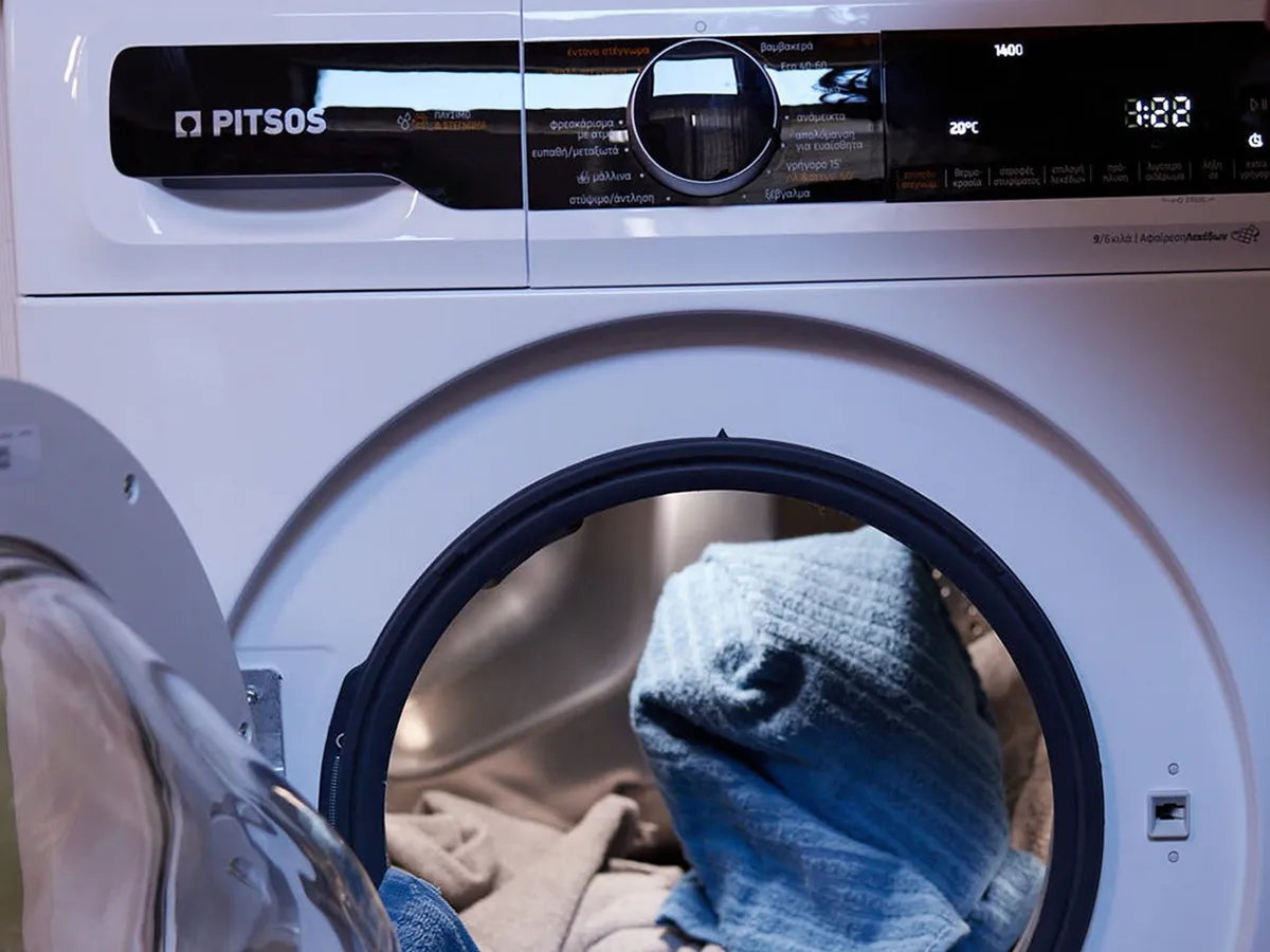 Φωτογραφία κοντινής λήψης ενός πλυντηρίου ρούχων με ορατό πίνακα ελέγχου και η πόρτα μπροστινής φόρτωσης, αποκαλύπτοντας μια μπλε πετσέτα στο εσωτερικό.