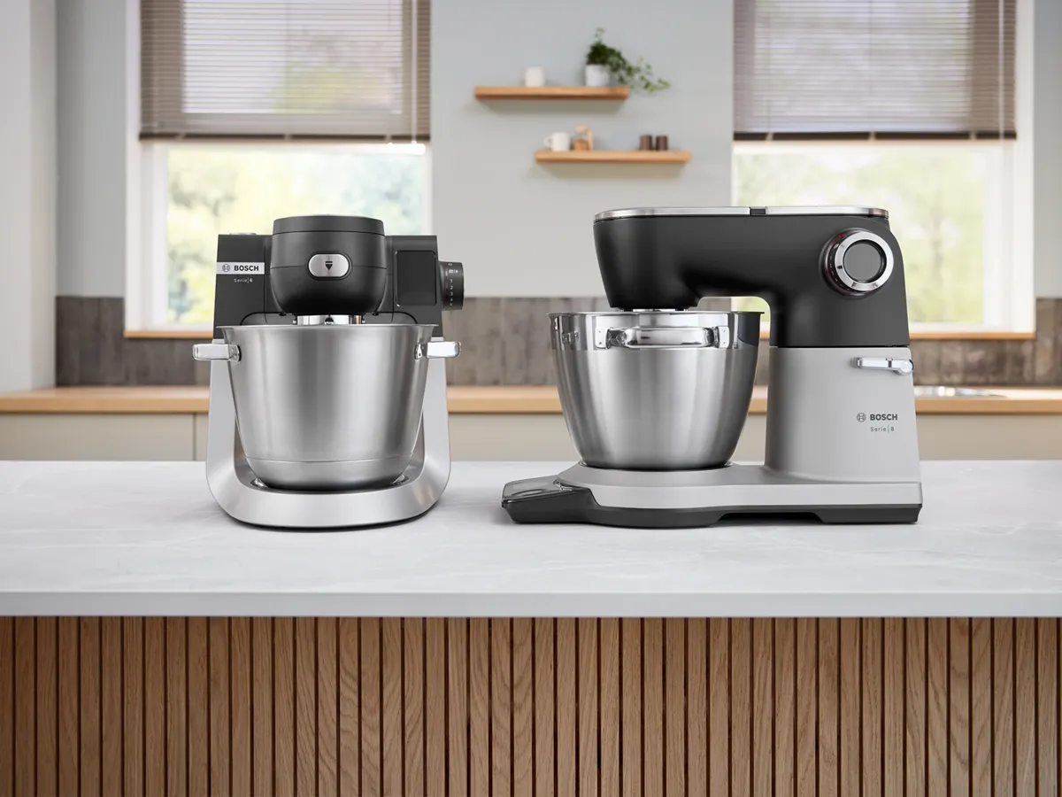 Two Bosch kitchen mixers with stainless steel bowls on a countertop in a modern kitchen setting.