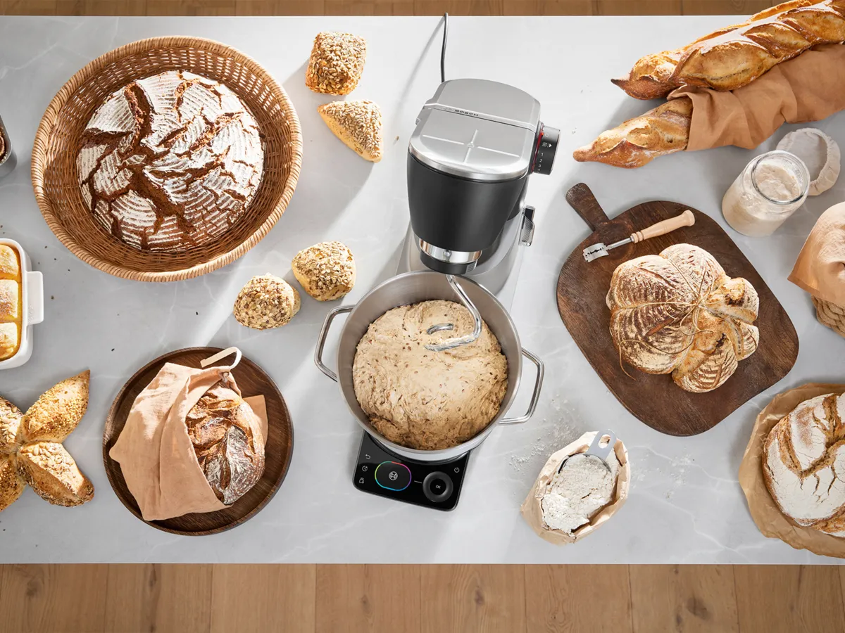 Kitchen countertop with stand mixer, dough, assorted breads, and baking ingredients.