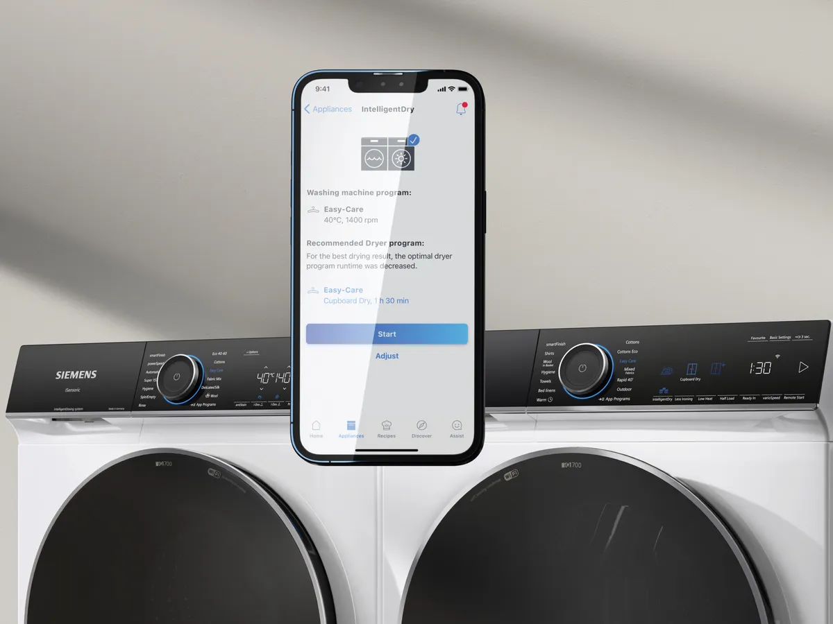 En smartphone visar torkprograminställningar placerade ovanför en modern tvättmaskin/torktumlare och visar upp smart hemteknik.