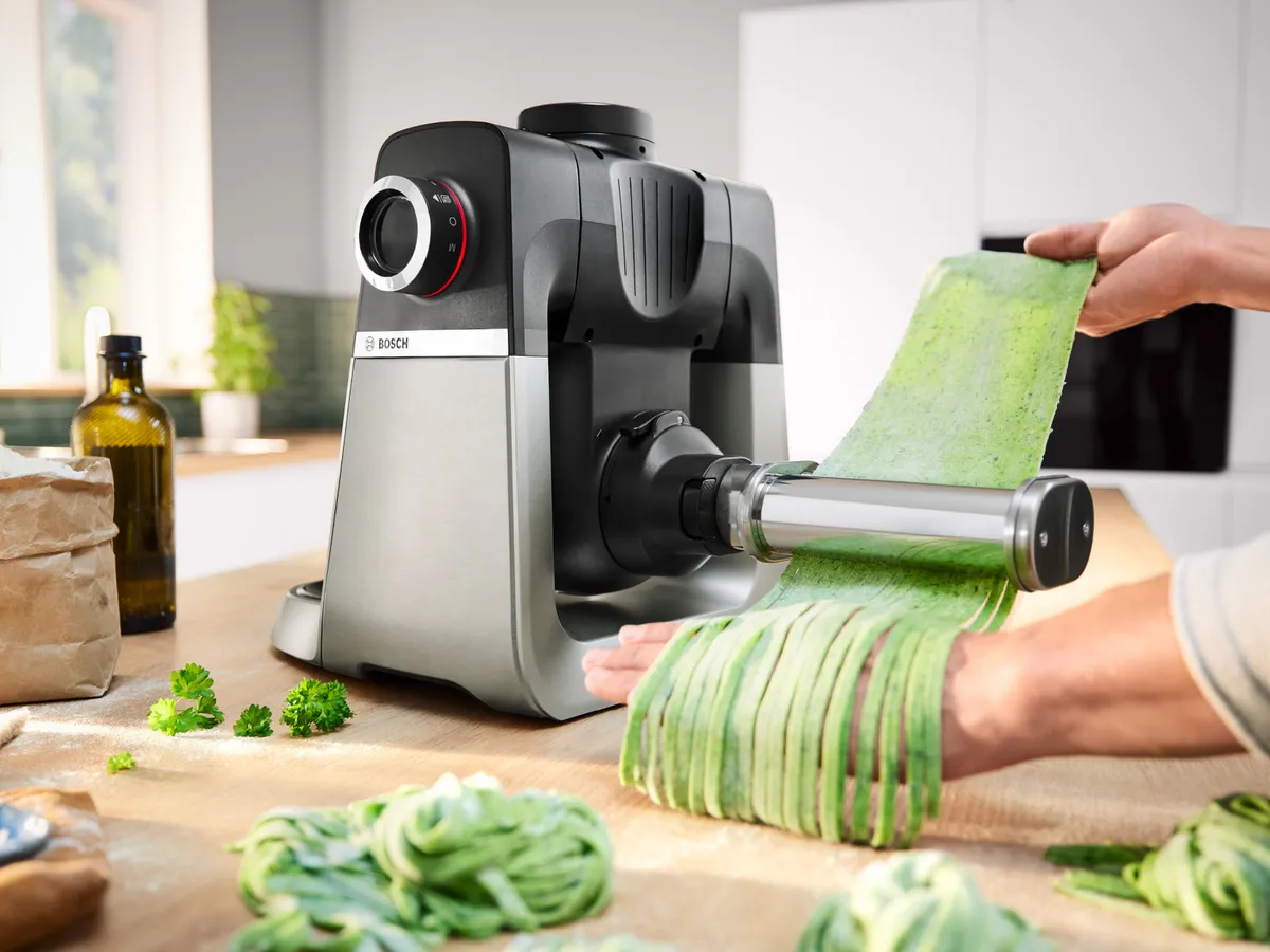 Stand mixer with PastaPassion attachment, with green pasta being fed through to make tagliatelle.