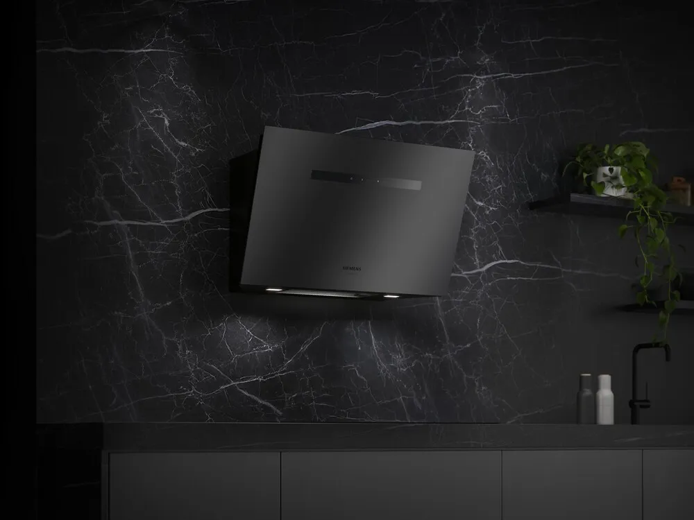 Een Siemens wandschouwkap in matte afwerking in een zwarte keuken met zwartmarmer achterwand.
