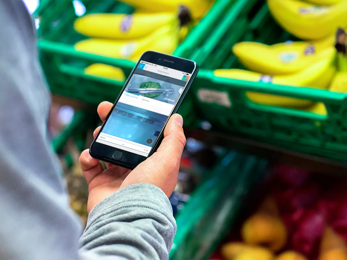 Person mit Smartphone, das Obst und Gemüse im Supermarkt zeigt.