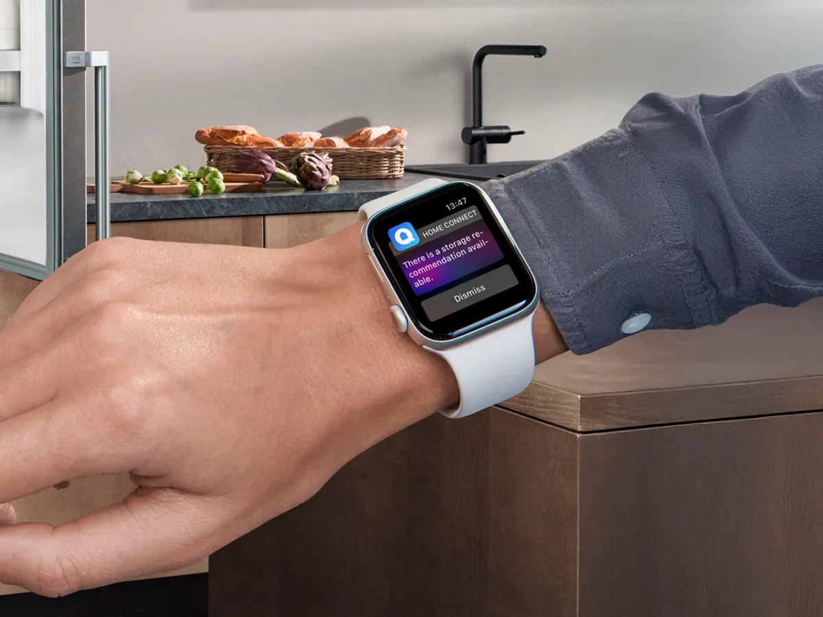 Wrist wearing a smartwatch displaying a Home Connect notification, with a modern kitchen in the background.