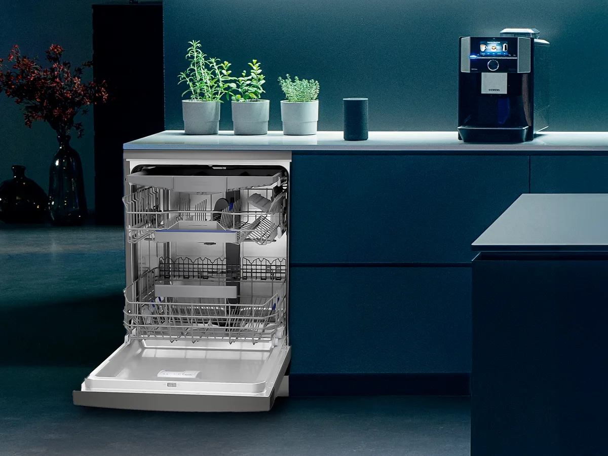 A Siemens opened dishwasher in the corner of a dark kitchen with plants and soft lighting.