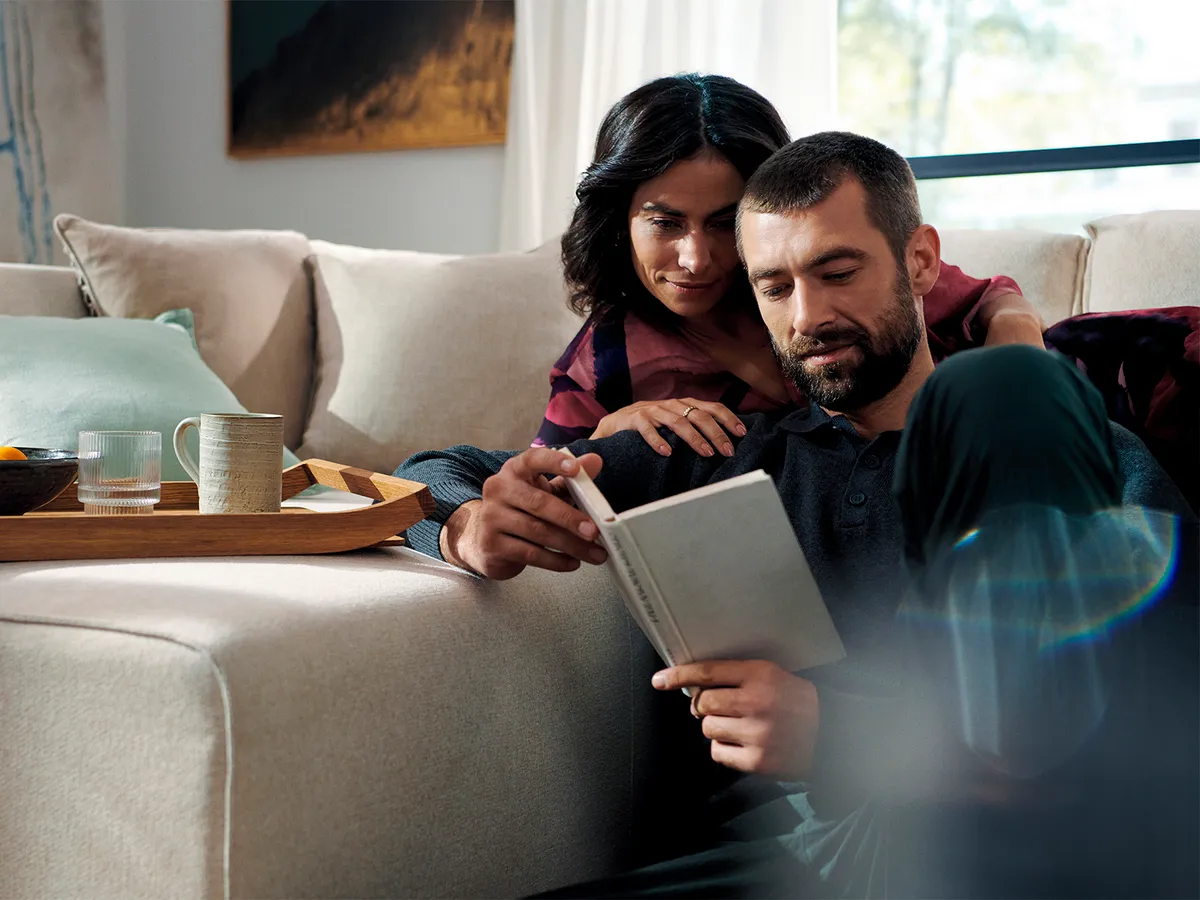 Couple relaxing on couch, using digital tablet, snacks and drinks on table.