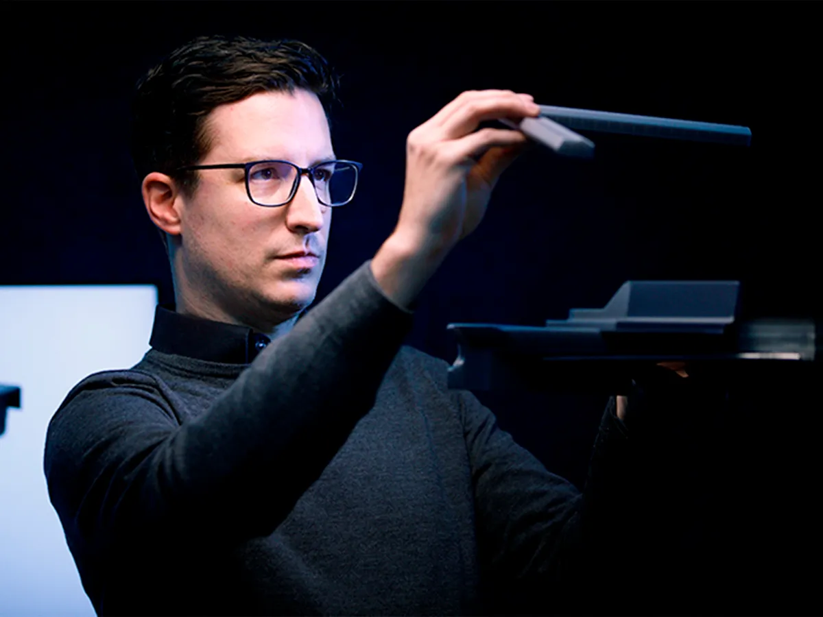 A male engineer wearing glasses and a polar neck top holding up an appliance part.