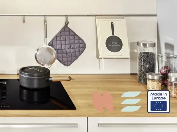 Küchentisch mit Kochutensilien, Topfpflanzen und Geräte auf einer Holzoberfläche.