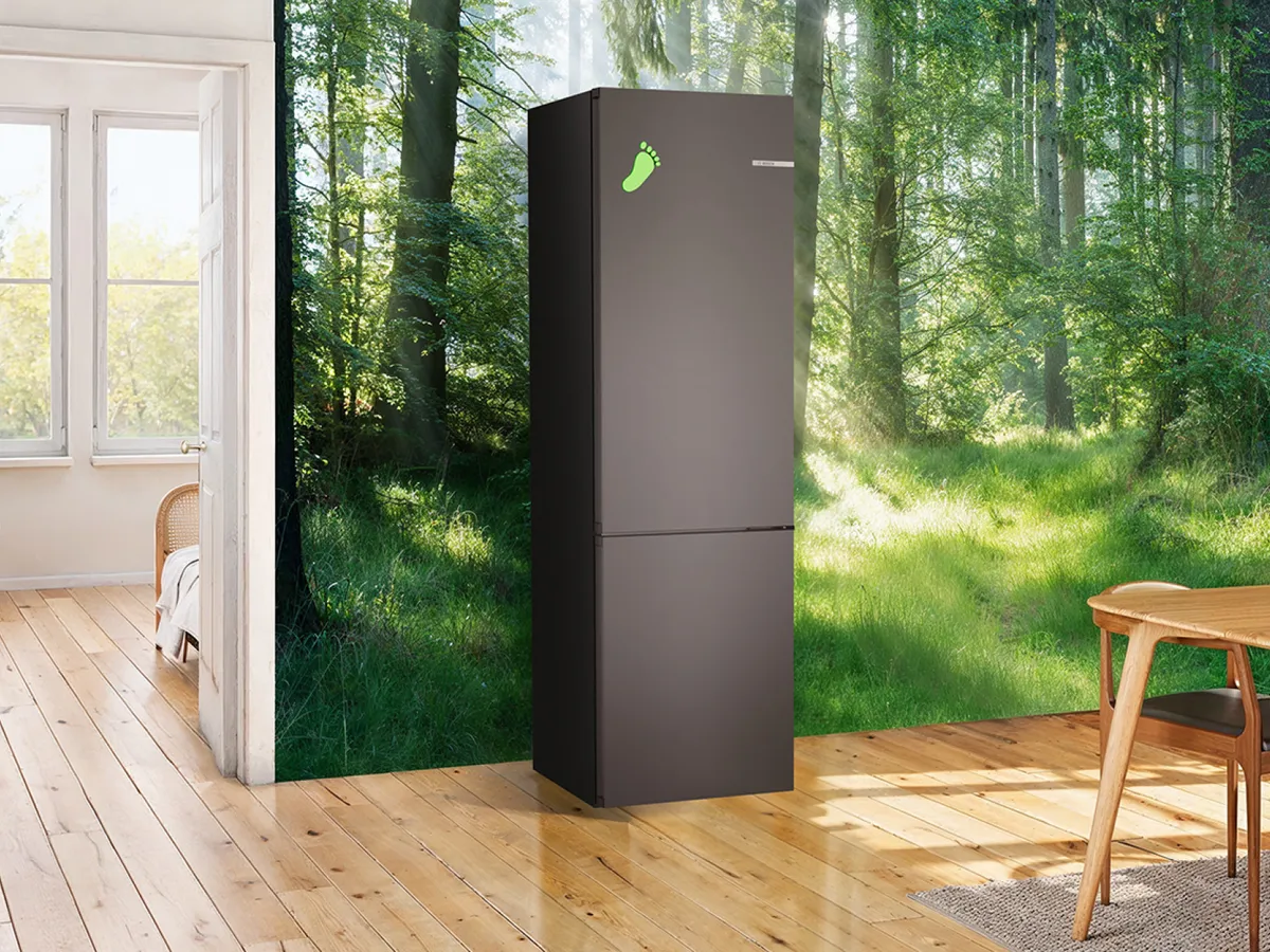 Cuisine lumineuse et spacieuse avec parquet, grandes fenêtres donnant sur une forêt luxuriante et réfrigérateur noir.