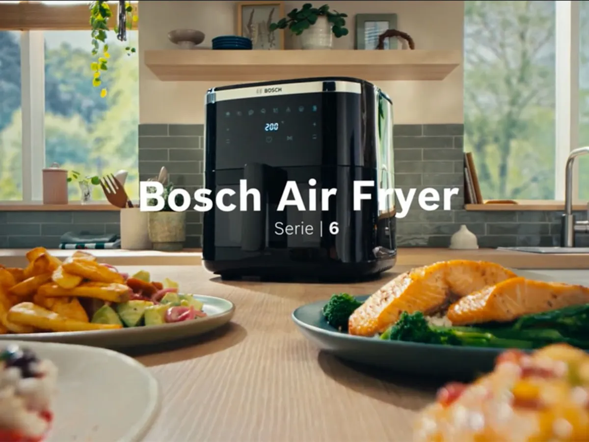 Bosch Air Fryer serije 6 s raznim jelima na drvenoj radnoj površini.