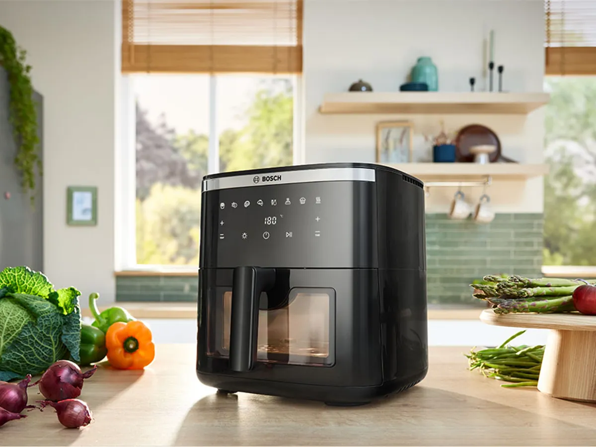 Bosch Air Fryer serije 6 na kuhinjskom pultu okružen svježim povrćem u svijetloj i modernoj kuhinji, spreman za pripremu jela.