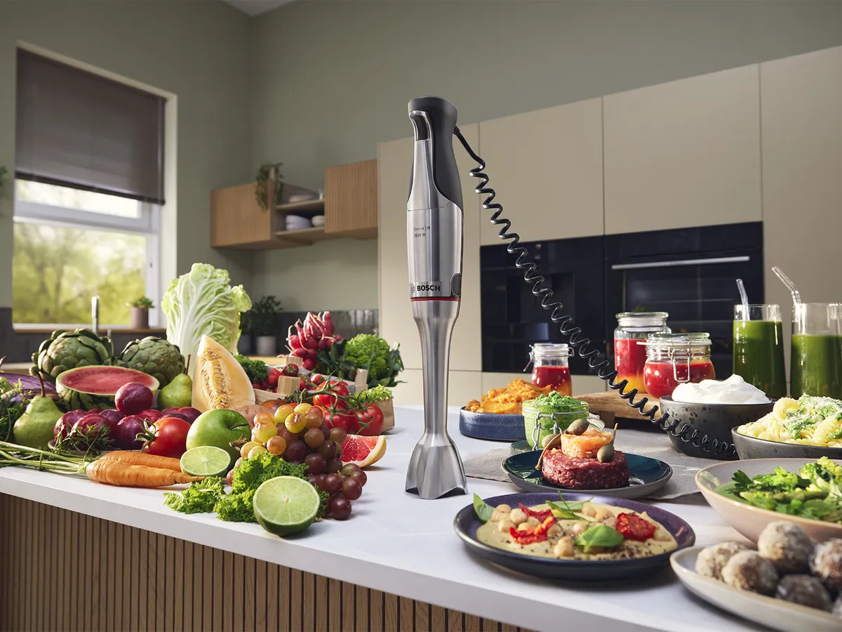 Bosch stavmixer ErgoMaster Series 8 på en köksbänk, omgiven av färsk frukt, grönsaker och färdigrätter som smoothies och dippsåser,