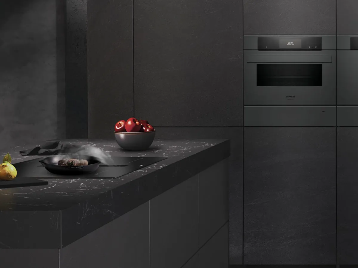A sleek black kitchen showcases modern design with a stovetop and steaming pan, highlighted by a bowl of red apples and a vibrant lemon.