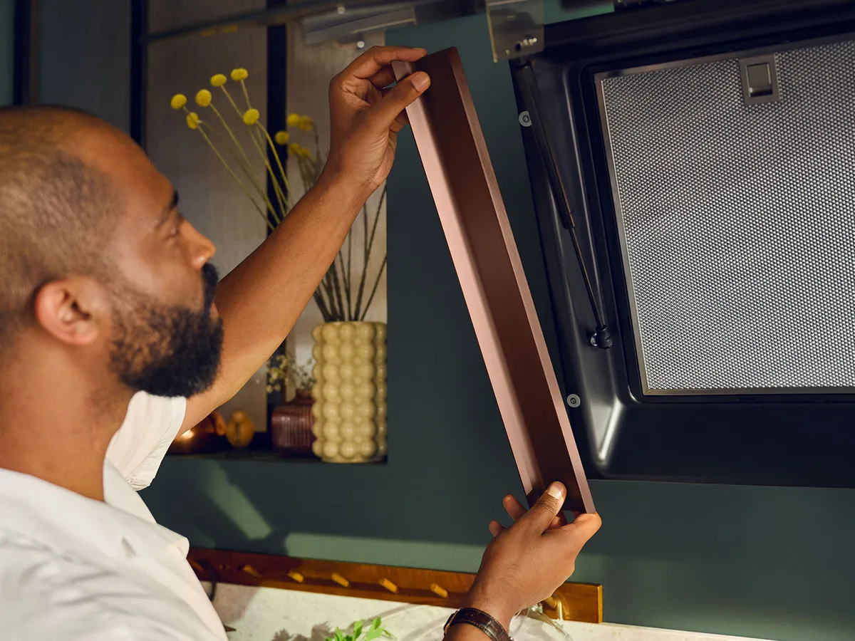 Un homme installe un panneau décoratif en bronze brossé sur sa hotte NEFF.