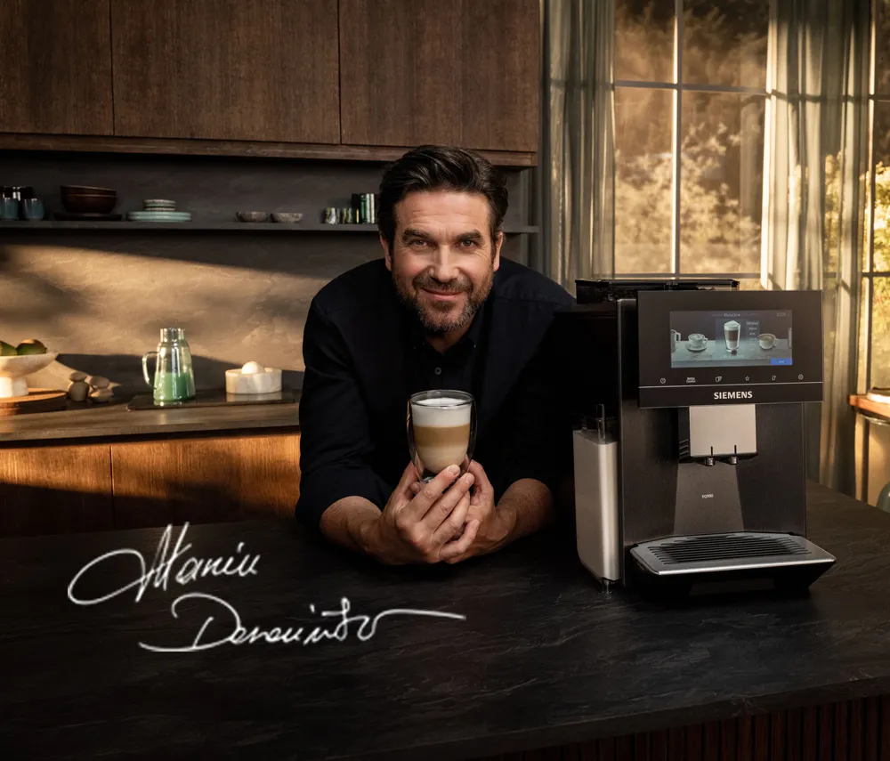 Mężczyzna trzymający filiżankę kawy obok ekspresu do kawy Siemens w eleganckiej kuchni z dużymi oknami
