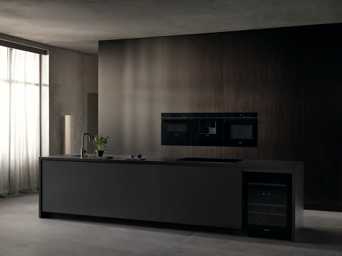 Sleek modern kitchen featuring a dark island, built-in appliances, and large windows with soft curtains allowing natural light.