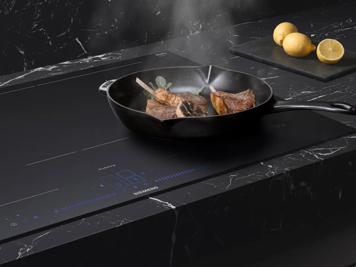 Sizzling meat on a black induction cooktop, paired with fresh lemons and a stylish marble countertop