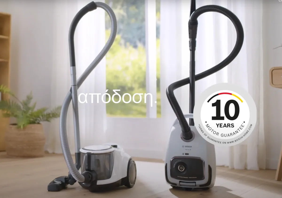 Δύο κυλινδρικοί σκουπάκοι Bosch χωρίς σακούλα στέκονται μπροστά από ένα παράθυρο σε μια μελέτη με τις λέξεις “απόδοση για όλες τις επιφάνειες” επάνω τους.