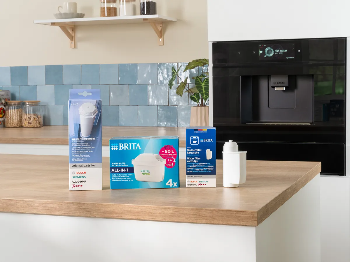 Quatre produits de filtration d’eau Brita sont posés sur un plan de travail en bois dans la cuisine, avec un mur en carrelage bleu clair et une machine à café en arrière-plan.