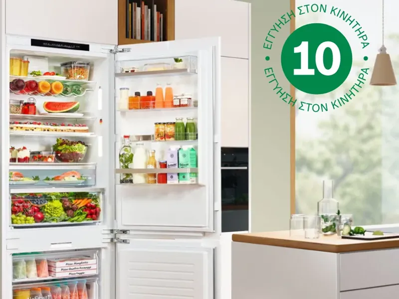 Ένας γεμάτος ανοιχτός ψυγεικαταψύκτης σε μια κουζίνα με λευκά έπιπλα και ξύλινο πάτωμα.