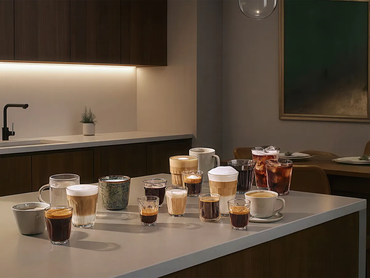 An assortment of coffee drinks in various glasses, including lattes, espressos, and iced coffee, arranged on a table.