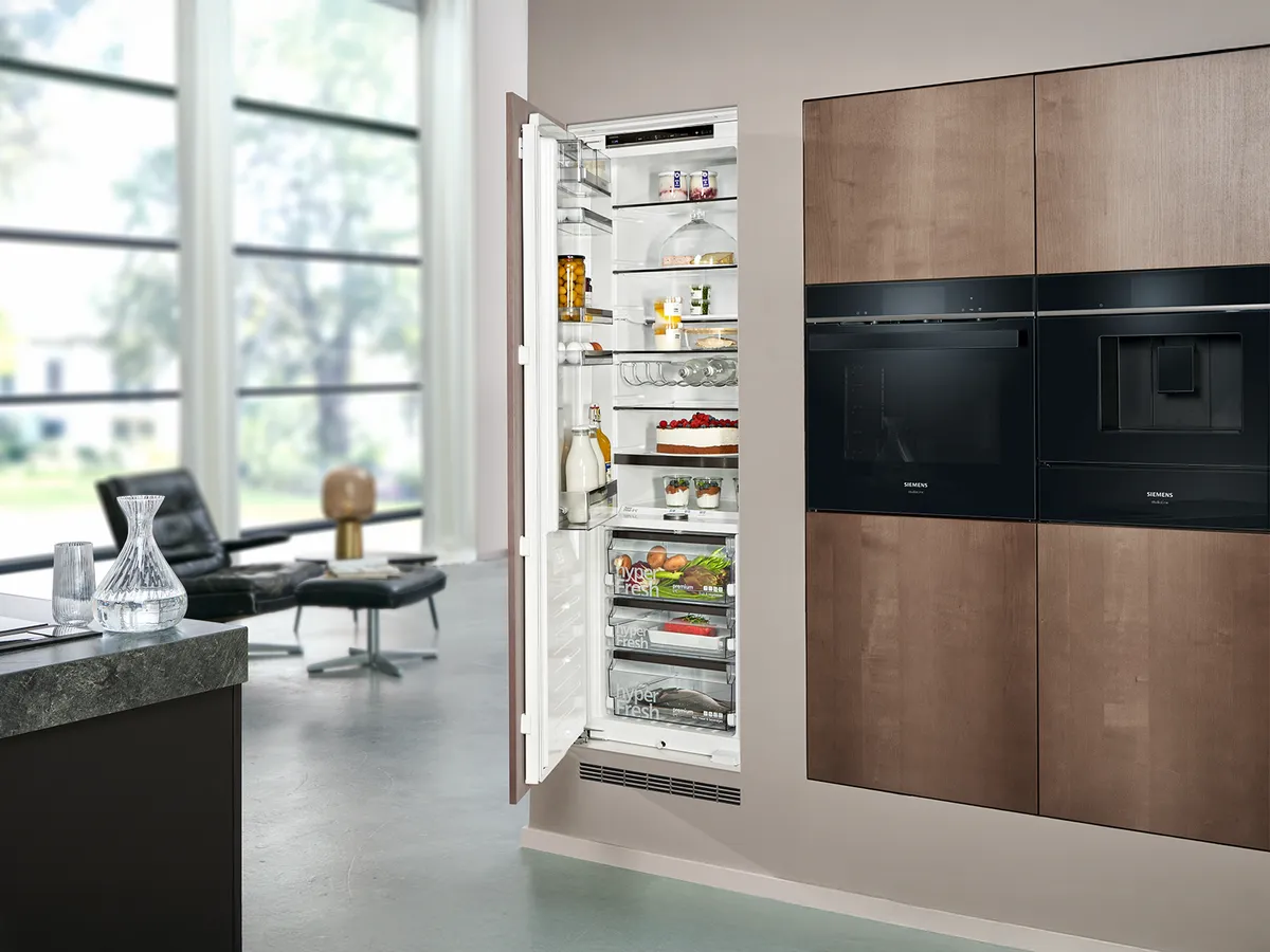 Modern kitchen with a spacious refrigerator open, showcasing organized food items, adjacent to stylish cabinets and a potted plant.