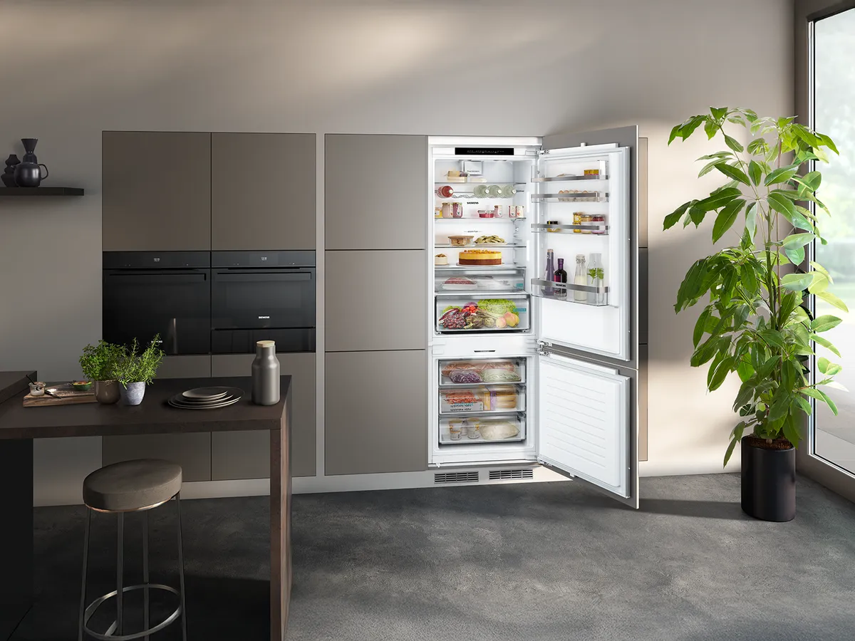 Modern kitchen with a spacious refrigerator open, showcasing organized food items, adjacent to stylish cabinets and a potted plant.