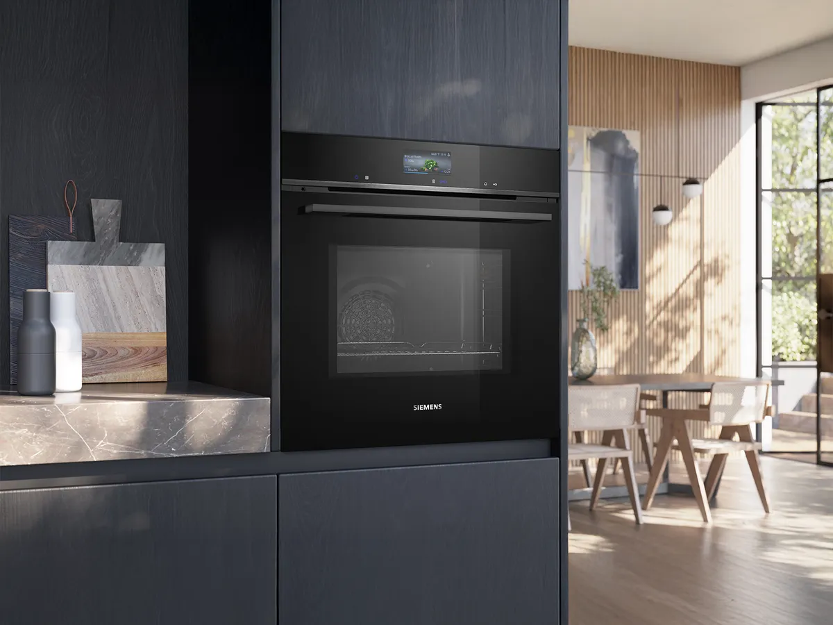 Modern kitchen with a sleek black Siemens oven, marble countertop, and a sunlit dining area in the background.